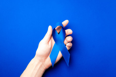November. Blue ribbon in hands isolated on deep blue background. Awareness prostate cancer of men health in November. Supporting people living and illnessの写真素材