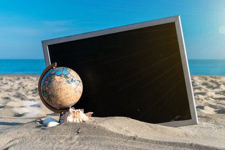 Summer sale. Globe, seashell, airplane and starfish near black desk on sea beach in sunny day. Copy space of summer vacation and business travel conceptの写真素材