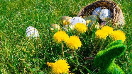 Easter eggs. Golden egg with yellow spring flowers in celebration basket on green grass background. Easter hunt conceptの写真素材