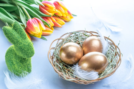 Easter Golden eggs in basket with spring tulips, white feathers on pastel blue background in Happy...