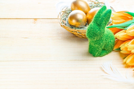 Easter eggs gold. Golden color egg in basket with spring tulips, white feathers on wooden background...