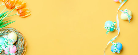 Easter background. Colorful egg with tape ribbon, spring tulips, feathers on pastel yellow background in Happy Easter decoration. Spring holiday top view bannerの写真素材