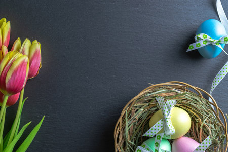 Easter background blue. Colorful egg with tape ribbon, spring tulips on dark rough stone background in Happy Easter decoration. Flat lay, top viewの写真素材