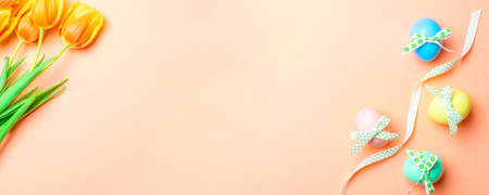 Easter bunny. Colorful egg with tape ribbon, spring tulips, feathers on pastel pink background in Happy Easter decoration. Traditional banner in top viewの写真素材