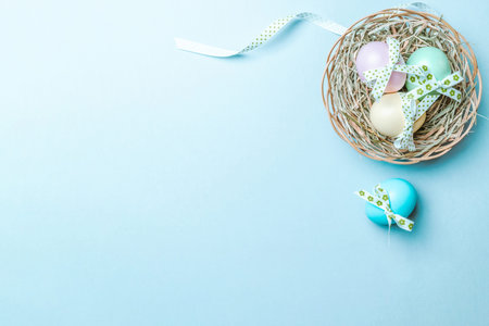 Golden easter color eggs in basket with spring tulips, white feathers on pastel blue background in...