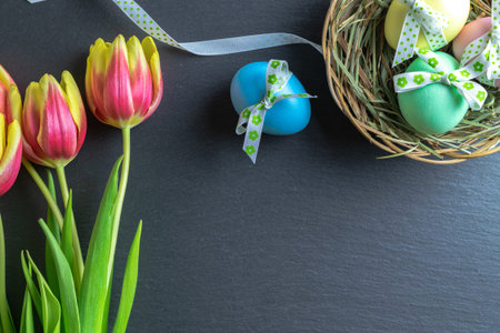 Easter bunny. Colorful egg with tape ribbon, spring tulips on dark rough stone background in Happy...