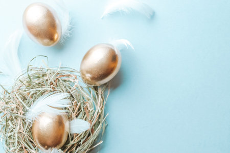 Golden easter color eggs in basket with white feathers on pastel blue background in Happy Easter...