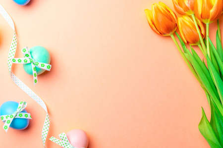 Easter message. Colorful egg with tape ribbon, spring tulips, feathers on pastel pink background in Happy Easter decoration. Foil minimalist egg design, modern top view templateの写真素材