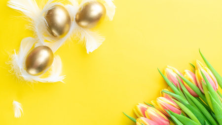Golden easter color eggs in basket with spring tulips, white feathers on pastel yellow background in...