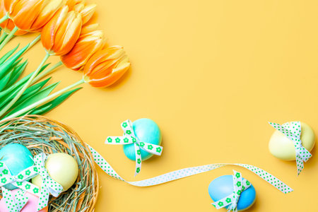 Egg color. Happy Easter decoration: Colorful egg with tape ribbon, spring tulips, white feathers on...