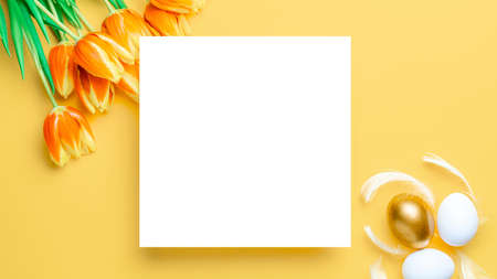 Easter frame. Golden, white color egg in basket with spring tulips, feathers on pastel yellow background in Happy Easter decoration. Festive design in flat layの写真素材