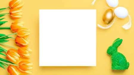 Easter flower. Golden, white color egg in basket with spring tulips, feathers on pastel yellow background in Happy Easter decoration. Festive design with copy spaceの写真素材