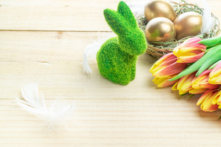 Easter eggs basket. Golden egg in basket with spring tulips, white feathers on wooden background in...