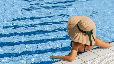 Swimming pool holidays. Happy young sexy girl in bikini swimsuit, sunglasses and straw hat in blue...
