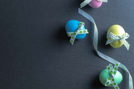 Easter background blue. Colorful egg with tape ribbon on dark rough stone background in Happy Easter decoration. Flat lay, top viewの写真素材