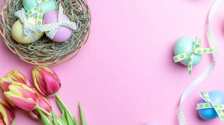 Easter Colorful egg with tape ribbon, spring tulips, white feathers on pastel pink background in Happy Easter decoration. Spring holiday flat lay conceptの写真素材