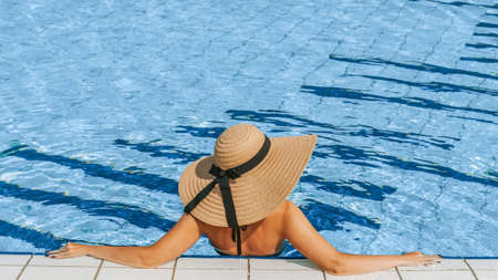 Pool party girl. Young sexy woman in straw hat, bikini swimsuit, sunglasses swimming in blue pool water. Resort spa in hotel on travel holidays vacationの写真素材