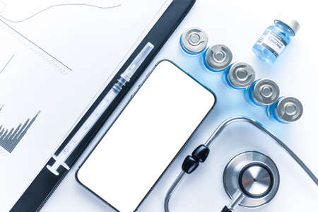 Medical application. Hospital equipment: doctor stethoscope, healthcare charts, syringe with needle and black smartphone with blank screen. Mockup generic deviceの写真素材