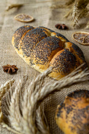 Whole wheat bread. Fresh loaf of rustic traditional bread with poppy seeds, wheat grain ear on linen texture background. Rye bakery with crusty loaves and crumbs. Homemade bakingの写真素材