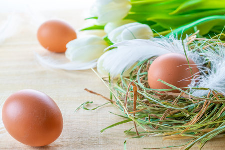 Natural easter color eggs in basket with spring tulips, white feathers on wooden table background in...