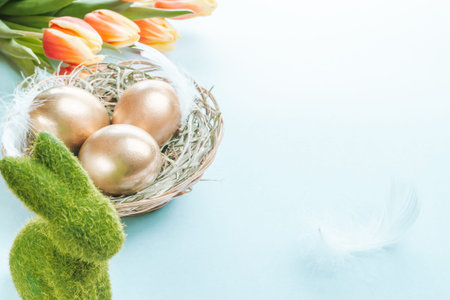 Easter Golden color eggs in basket with spring tulips, white feathers on pastel blue background in...