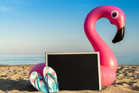 Sea background. Funny pink toy flamingo with blackboard, slippers for text on summer ocean nature beach background in sunny tropical day. Luxury lifestyle travelの写真素材