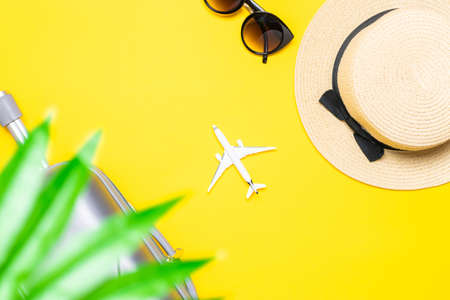 Summer holidays background. Womens accessories traveler: suitcase, white plane, sunglasses on yellow background with empty space for text. Exotic tropical beach with copy spaceの写真素材