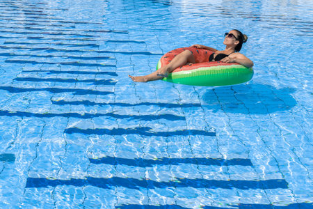 Swimming pool holidays. Happy young sexy girl in bikini swimsuit, sunglasses and inflatable rubber...