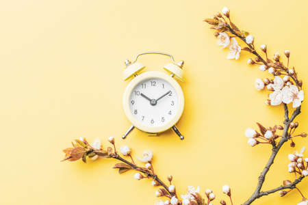 Spring background flowers. April floral nature and spring sakura blossom with alarm clock on soft yellow background. Banner for 8 march, Happy Easter with place for text. Springtime conceptの写真素材