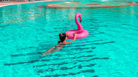Summer sale. Girl swimming with Pink inflatable flamingo in pool water for summer beach background....