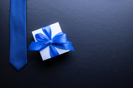 Fathers gift. White box with bow ribbon, blue bowtie or tie on dark background. Concept of Fathers Day greeting card, copy space for textの写真素材