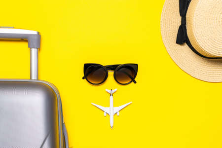 Summer pattern background. Suitcase, sunglasses with palm leaves and straw hat, white plane in travel composition on yellow background. Top view, flat lay. Copy spaceの写真素材