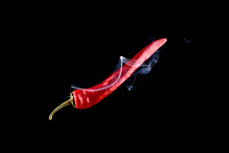 Chilli peppers isolated. Spicy chile cayenne pepper with abstract fog or steam mist cloud. Red hot chili paprika with tongue of fire flame on black background. Fresh spice vegetable conceptの写真素材