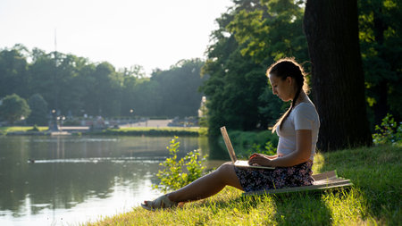 Work laptop outdoor. Student woman with computer, tablet in summer nature park. Girl does business with online technology outside. Electronic gadgets distance learning conceptの写真素材