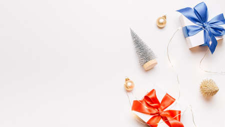 Christmas gift. White gift with red bow, gold balls and sparkling lights garland in xmas decoration on white background for greeting card. Xmas backdrop with space for textの写真素材