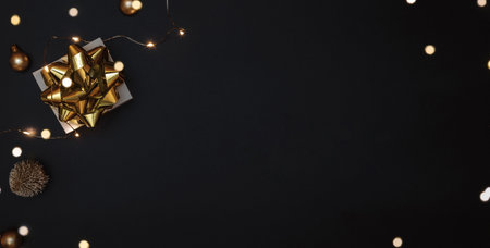 Christmas gift. White gift with golden bow, gold balls and sparkling lights garland in xmas decoration on dark background for greeting card. Xmas backdrop with space for textの写真素材