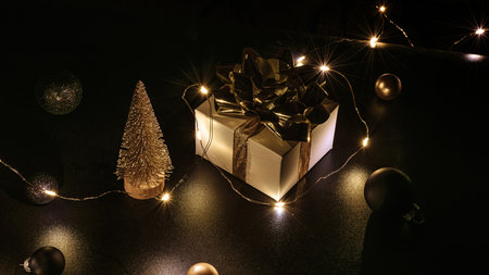 Holiday Christmas background. White gift box with golden ribbon, New Year balls and sparkling lights garland in xmas composition on black for greeting card. Winter holidays, New Year.の写真素材