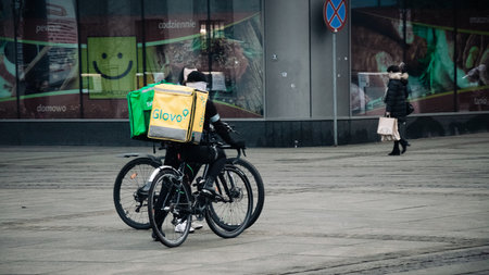 KATOWICE. POLAND - March 26, 2021: Driver man on bike or motorcycle for fast restaurant deliver. Food courier bag for delivery takeaway service. Glovo courier on scooter delivering foodのeditorial素材