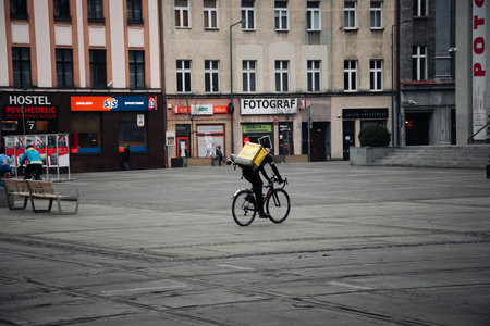 KATOWICE. POLAND - March 26, 2021: Driver man on bike or motorcycle for fast restaurant deliver. Food courier bag for delivery takeaway service. Glovo courier on scooter delivering foodのeditorial素材