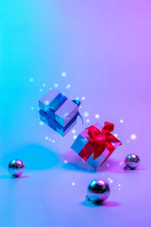 Neon Christmas winter background. Xmas gift box with shine lights. Holiday gifts, decoration bauble ball on neon abstract gradient backdrop. Happy new year copy spaceの写真素材