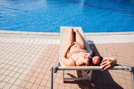 Pool party girl. Happy young sexy girl in bikini swimsuit, sunglasses on resort chair. Relax lounge at luxury hotel blue water pool. Resort spa in hotel on travel holidays vacationの写真素材