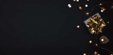 Christmas gift. White gift with golden bow, gold balls and sparkling lights garland in xmas decoration on dark background for greeting card. Xmas backdrop with space for textの写真素材