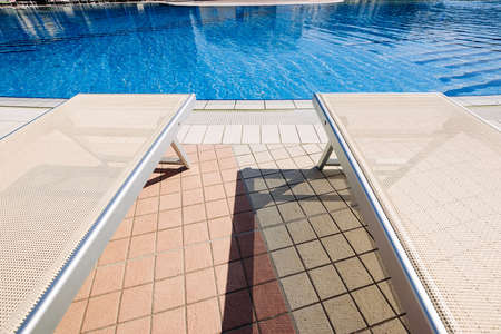 Resort pool. Summer resort chair, relax lounge at luxury hotel pool. Beach lounger chaise. Vacation sunbed. Blue water, sunny happy travel holidayの写真素材