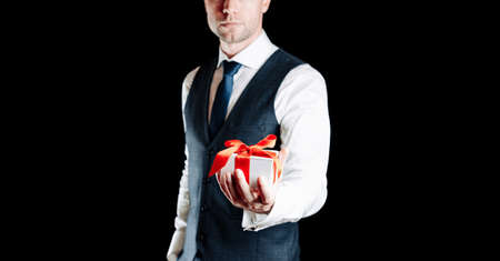 Gift box hand. Happy young business man holding surprise giftbox present with red ribbon isolated on black background. Valentines day, Christmas, New Year banner with copy spaceの写真素材
