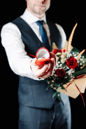 Love propose. Diamond engagement ring, red roses bouquet in young happy man hands. Marriage proposal. Marry me conceptの写真素材
