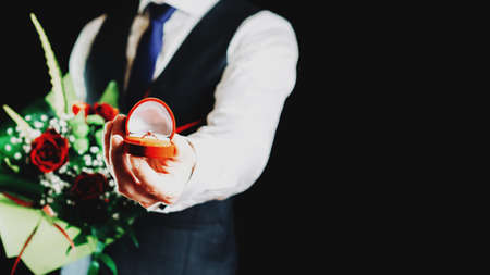 Love propose. Diamond engagement ring, red roses bouquet in young happy man hands. Marriage proposal. Marry me conceptの写真素材