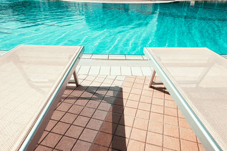 Resort pool. Summer resort chair, relax lounge at luxury hotel pool. Beach lounger chaise. Vacation sunbed. Blue water, sunny happy travel holidayの写真素材