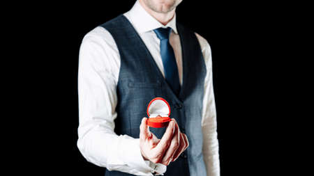 Marry me. Young happy man holding red gift box with diamond engagement ring, red roses bouquet. Engagement marriage ringの写真素材