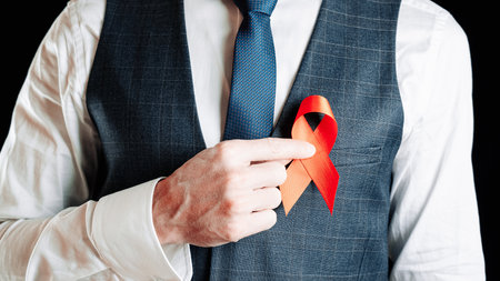 Aid ribbon silk. Red ribbon in hiv world day in man hand. Awareness aids and cancer symbol on black background. HIV, AIDS and aging awareness month with copy spaceの写真素材