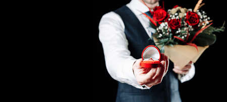 Marriage proposal. Diamond engagement ring, red roses bouquet in young happy man hands. Diamond ring propose in Valentine Dayの写真素材